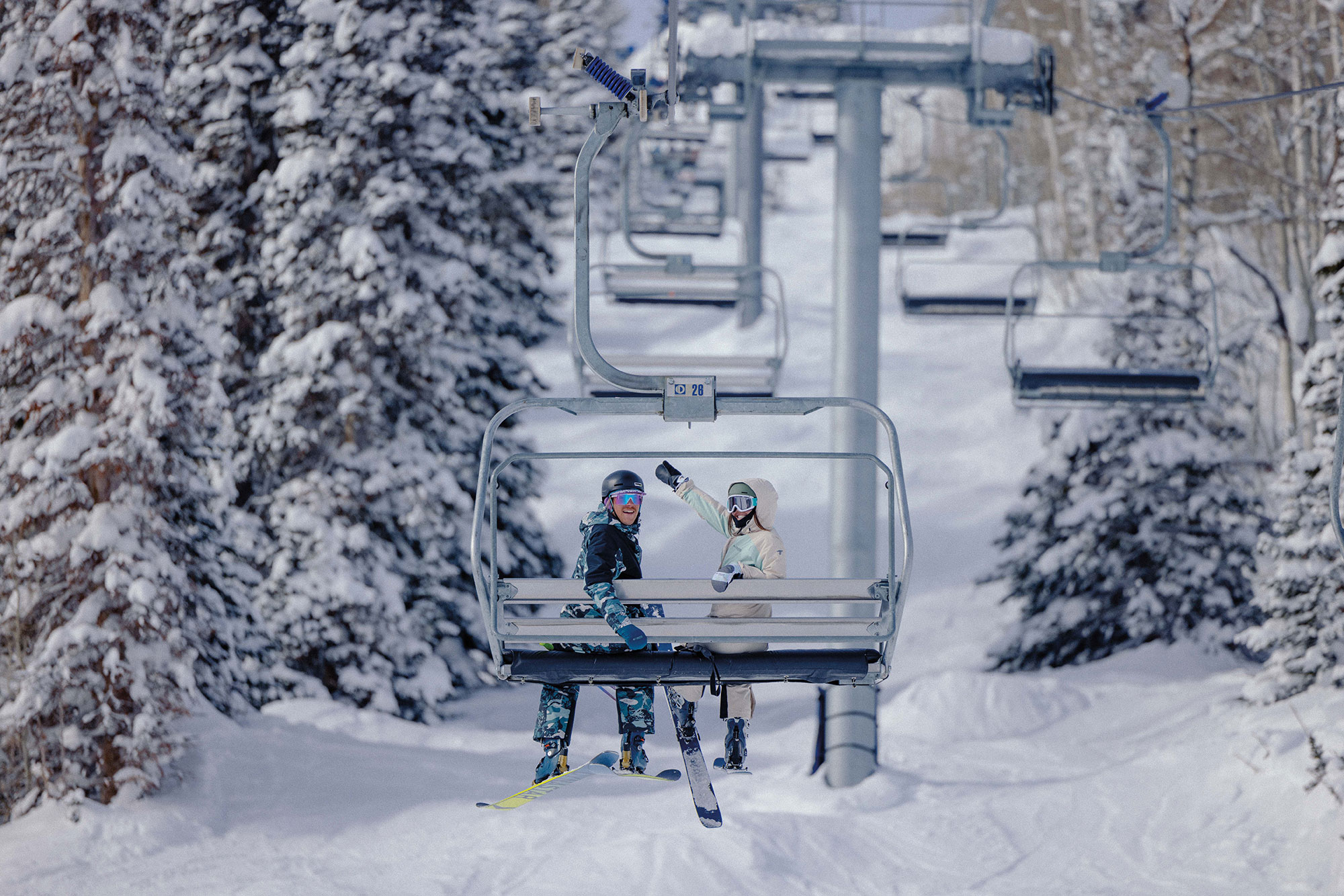 Due persone sedute su una seggiovia in un paesaggio innevato che indossano la Columbia Titanium Ski Collection